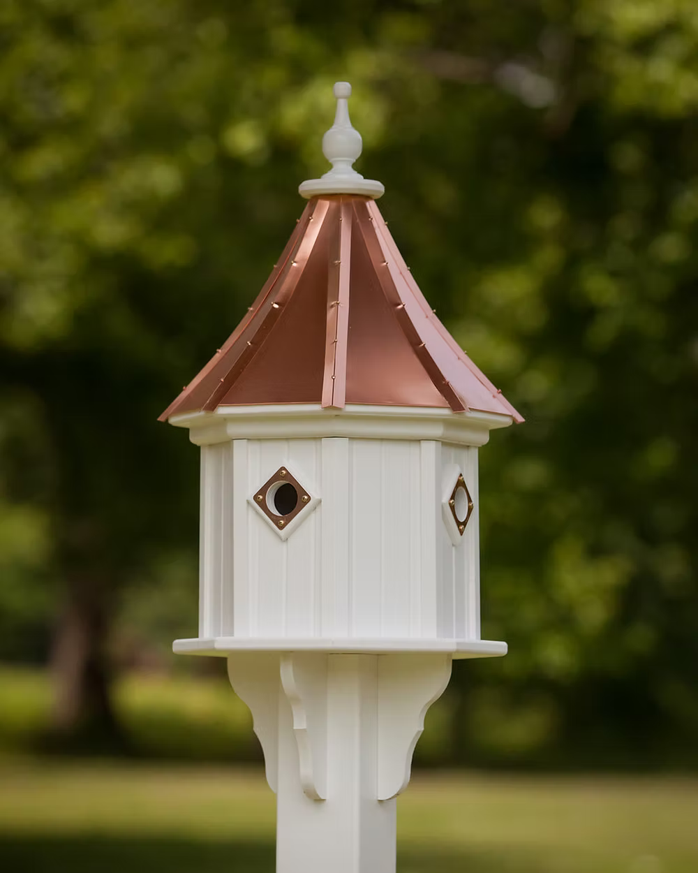 White birdhouse with a copper roof against a blurred green background