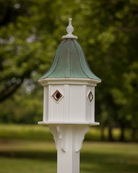 White birdhouse with green copper roof against a blurred green background