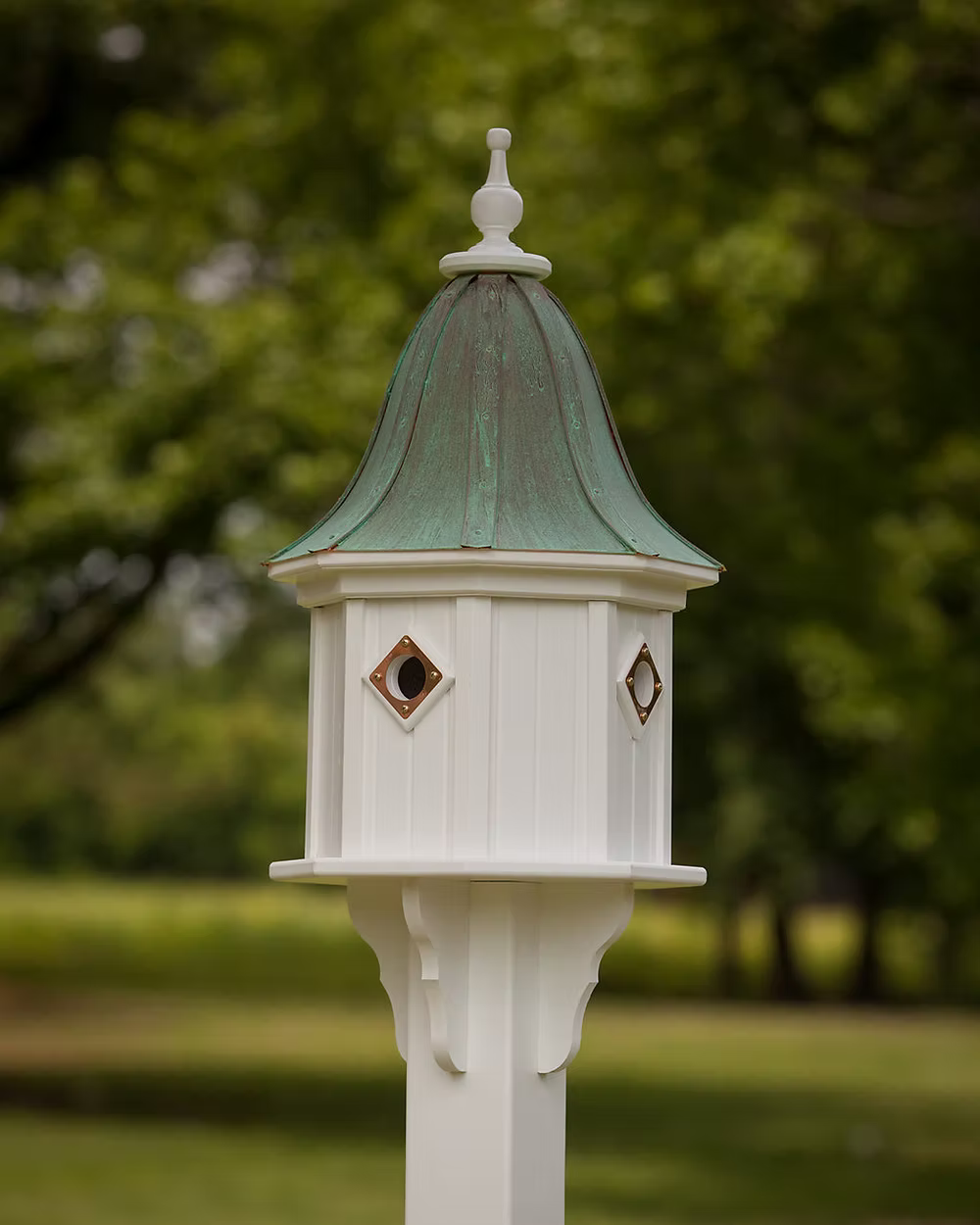 White birdhouse with green copper roof against a blurred green background