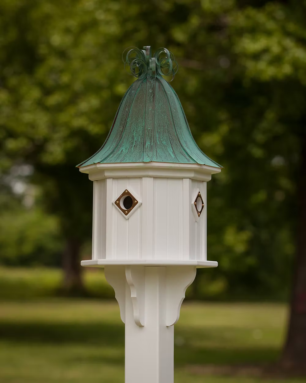 Decorative white birdhouse with a green copper roof in a garden setting