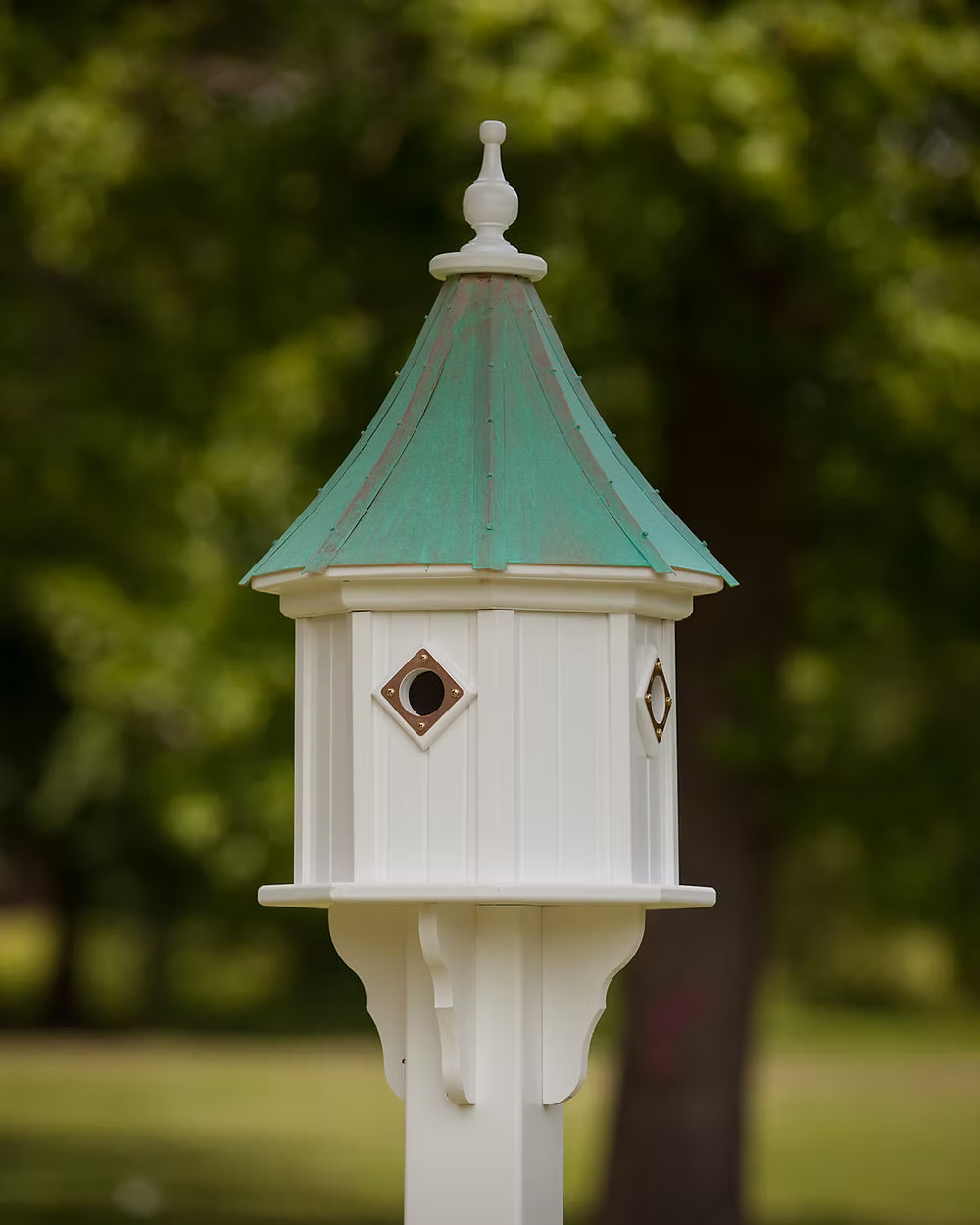 White birdhouse with a green roof against a blurred green background