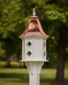 Decorative white birdhouse with a copper roof against a blurred green outdoor background