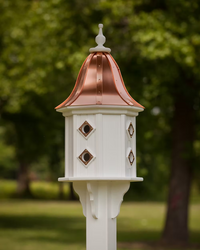 Decorative white birdhouse with a copper roof against a blurred green outdoor background