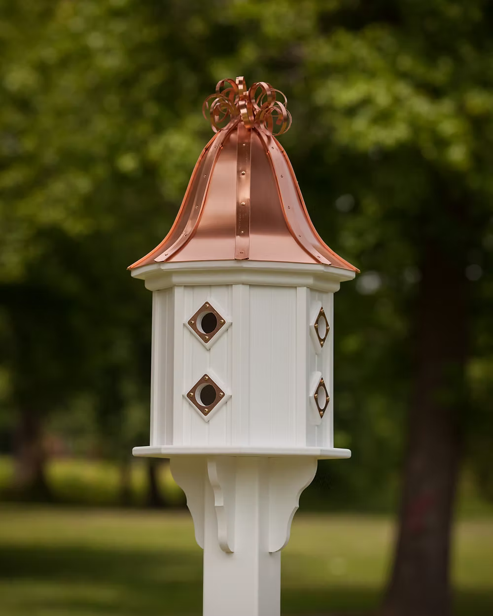 White birdhouse with copper roof and decorative elements against a blurred green outdoor background
