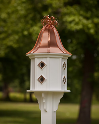 White birdhouse with copper roof and decorative elements against a blurred green outdoor background