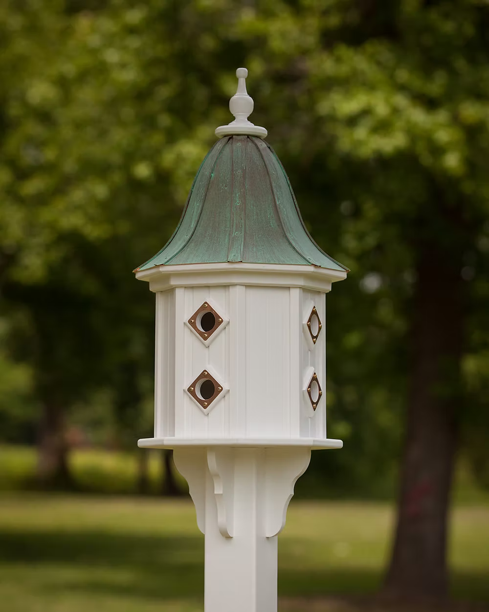 White birdhouse with green copper roof against a blurred green outdoor background