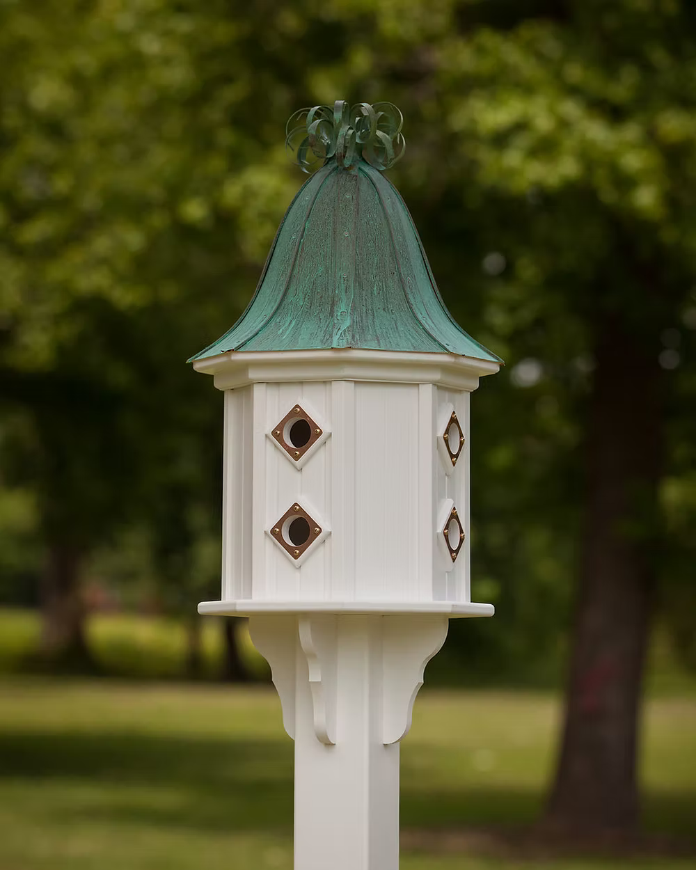 White birdhouse with a green copper roof against a blurred green outdoor background
