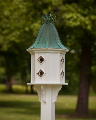 White birdhouse with a green copper roof against a blurred green outdoor background