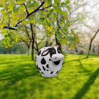 Cow-shaped bird house hanging from a tree in a park