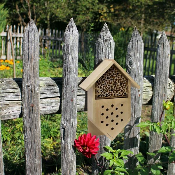 Beeswax bee house attached to a wooden fence with flowers in the background