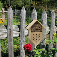 Beeswax bee house attached to a wooden fence with flowers in the background