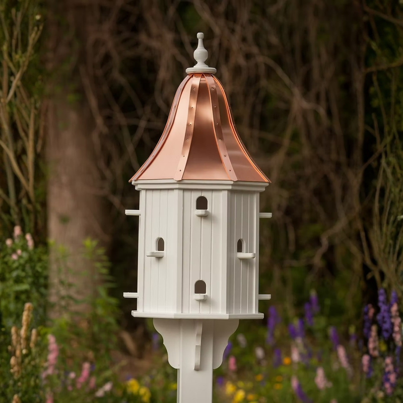 Gorgeous white birdhouse with multiple perch entries and a bell shaped copper roof in a garden setting