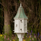Decorative birdhouse with multiple perch entry points and a patina copper roof in a garden setting