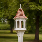 Decorative bird feeder with a copper roof in a garden setting