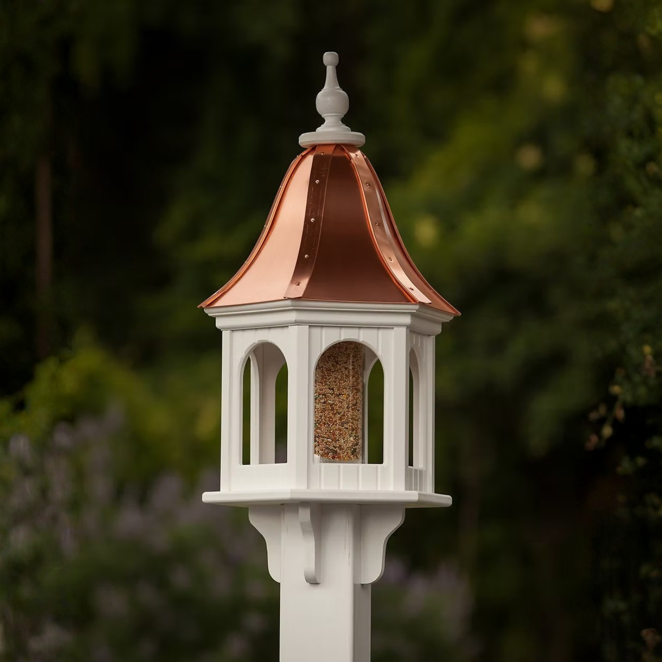 Decorative bird feeder with copper roof against a blurred natural background