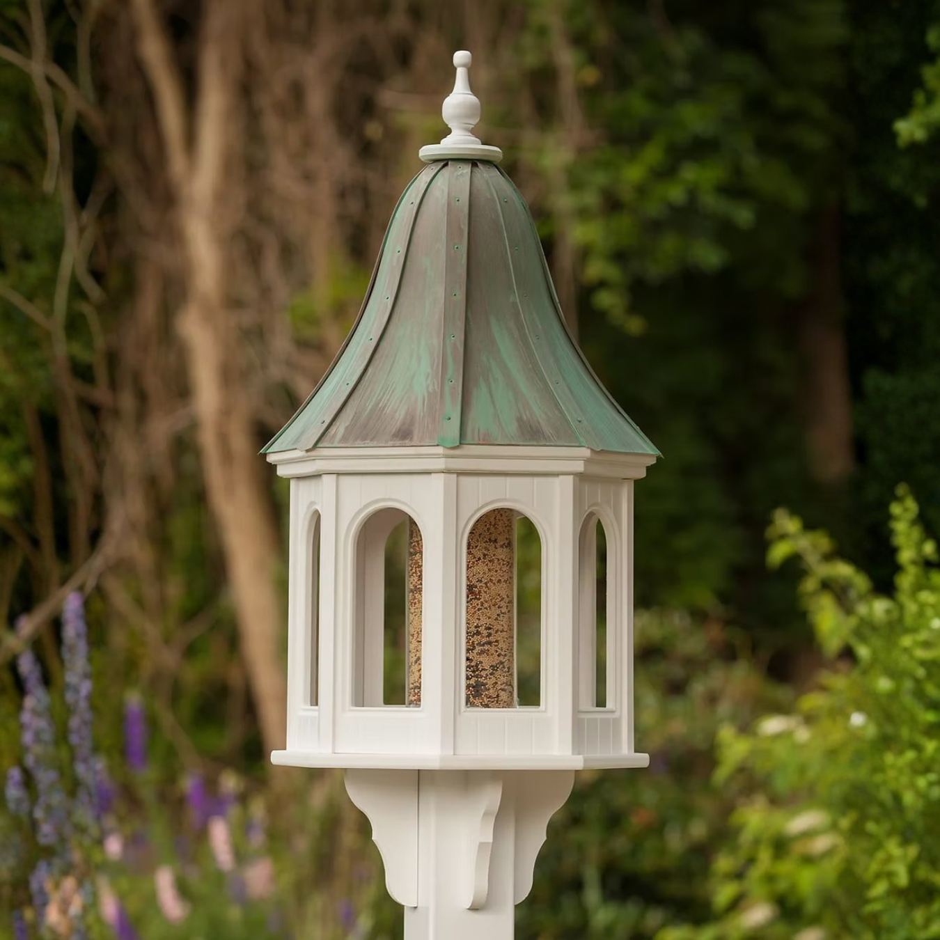 Decorative bird feeder with a patina copper roof and white base in a garden setting