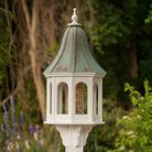 Decorative bird feeder with a patina copper roof and white base in a garden setting