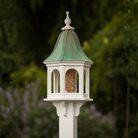 Decorative bird feeder with patina copper roof and white base against a blurred natural background