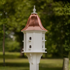 White decorative birdhouse with a bell shaped copper roof in a garden setting