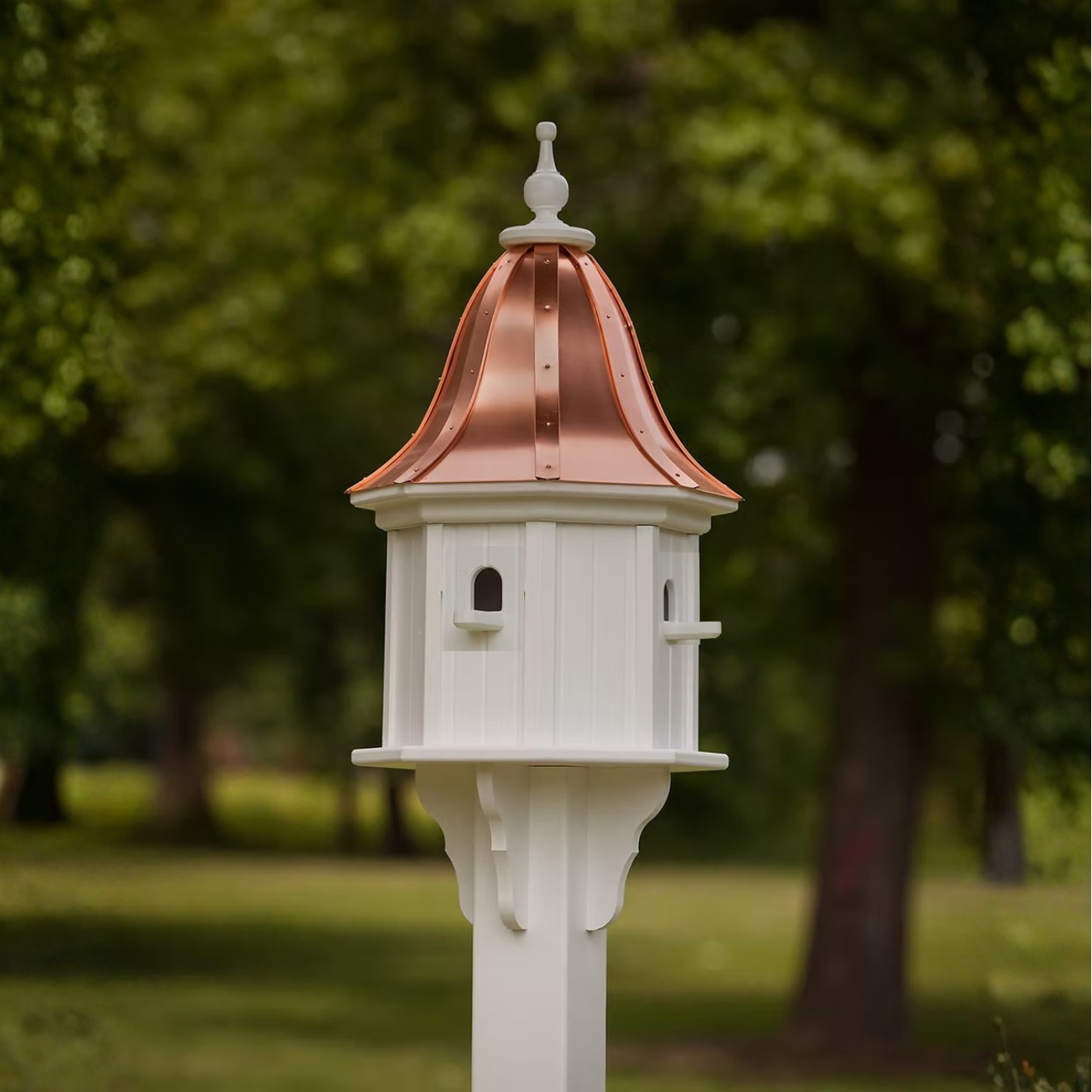 Decorative white birdhouse with a bell shaped copper roof in a garden setting