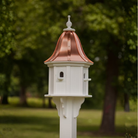Decorative white birdhouse with a bell shaped copper roof in a garden setting