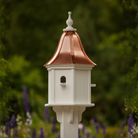 Decorative white birdhouse with bell shaped copper roof in a blurred green garden