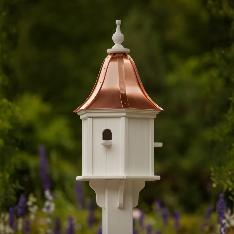 Decorative white birdhouse with bell shaped copper roof in a blurred green garden