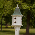 Decorative white birdhouse with a patina copper roof against a blurred green outdoor background