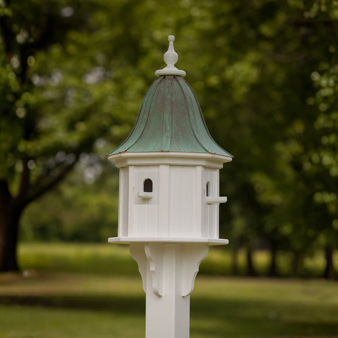 Decorative birdhouse on a stand with a bell shaped patina copper roof in a blurred green garden background