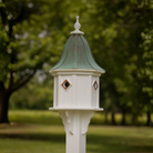 Decorative birdhouse with copper portals and a bell shaped patina copper roof with a blurred green outdoor background