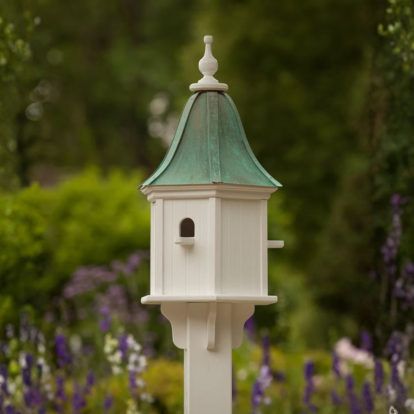 Decorative birdhouse with a bell shaped patina copper roof in a garden setting