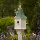 Decorative birdhouse with a bell shaped patina copper roof in a garden setting