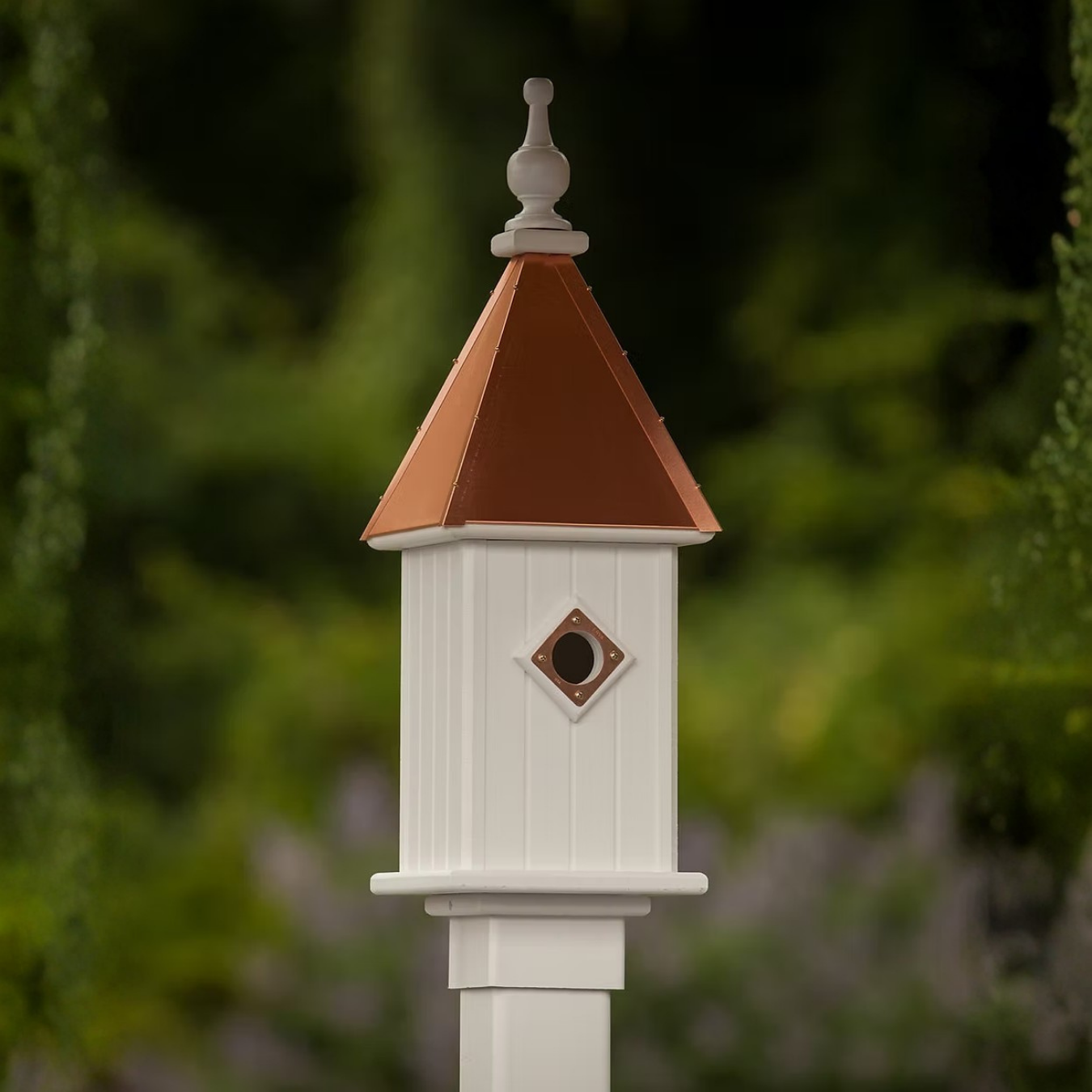 White birdhouse with a copper roof against a blurred green background