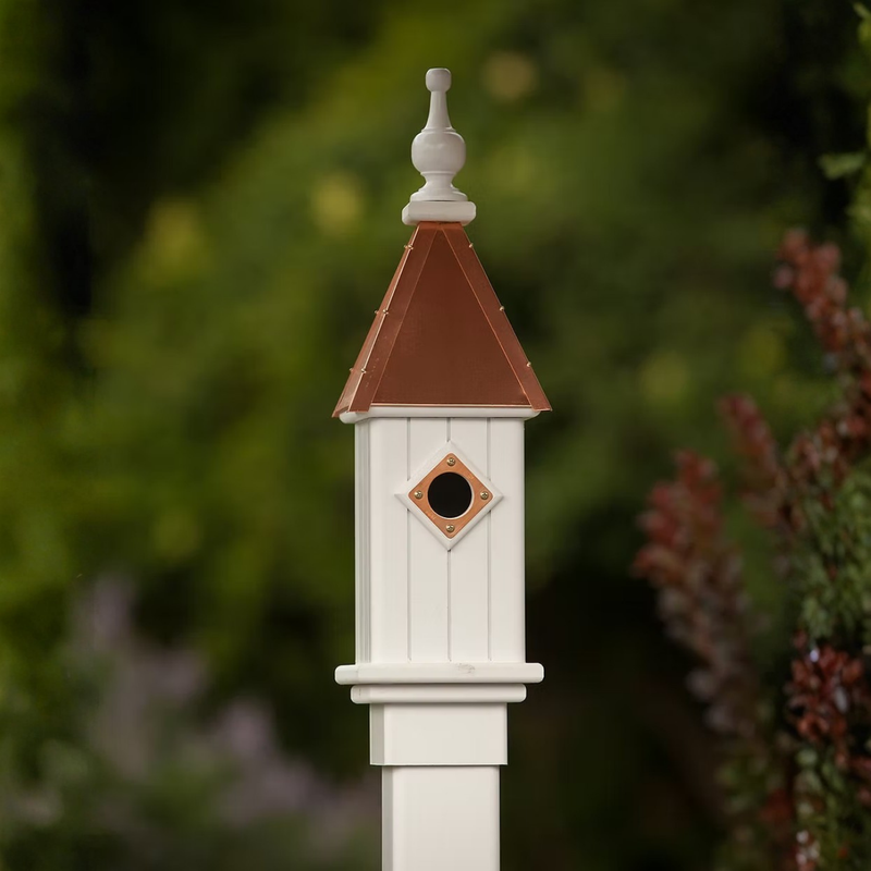 White birdhouse with a copper roof against a blurred green background