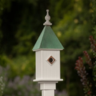 White birdhouse with a patina copper roof against a blurred natural background