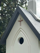 Birdhouse with a cross on top against a blurred green background