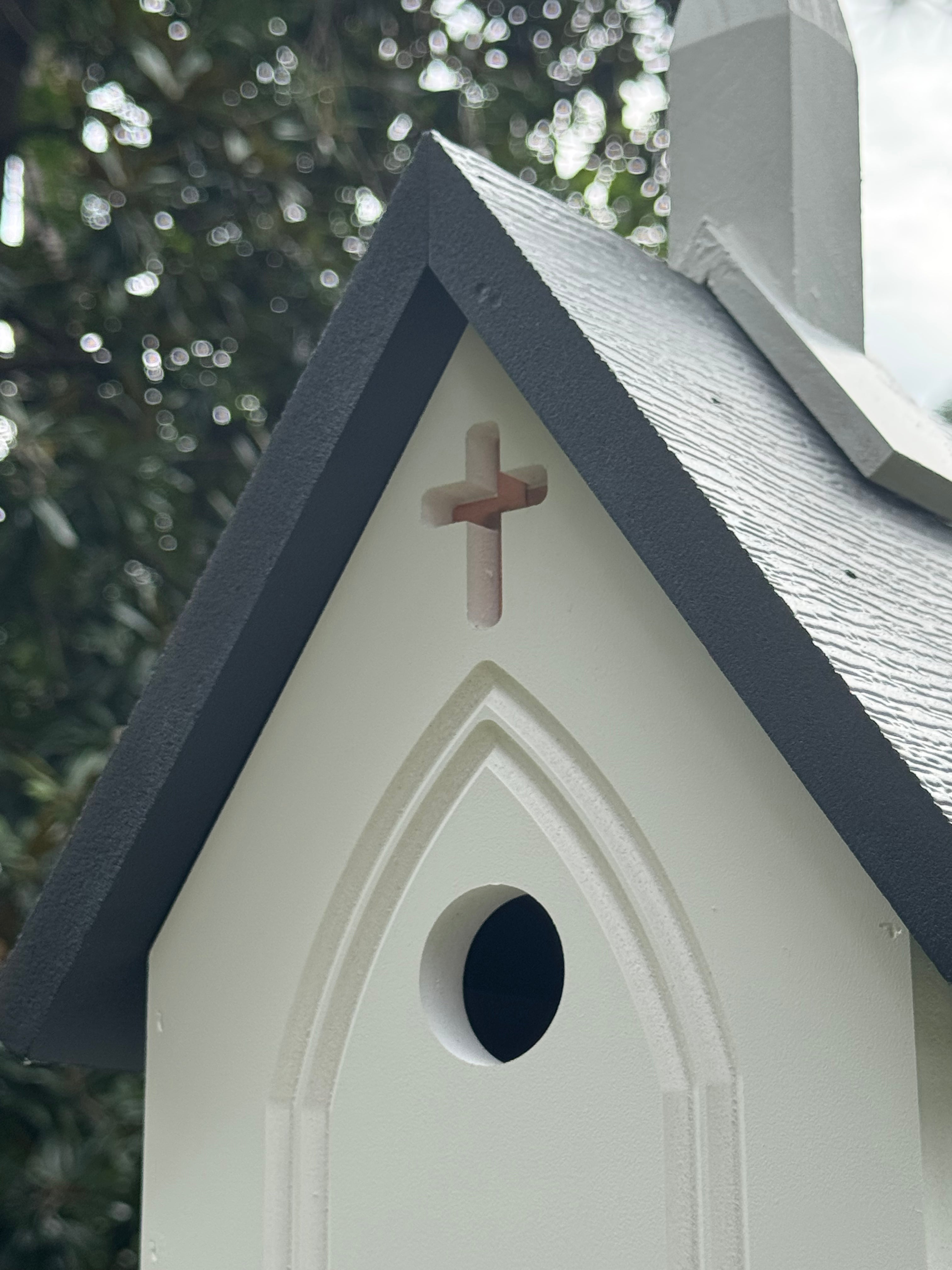 Birdhouse with a cross on top against a blurred green background