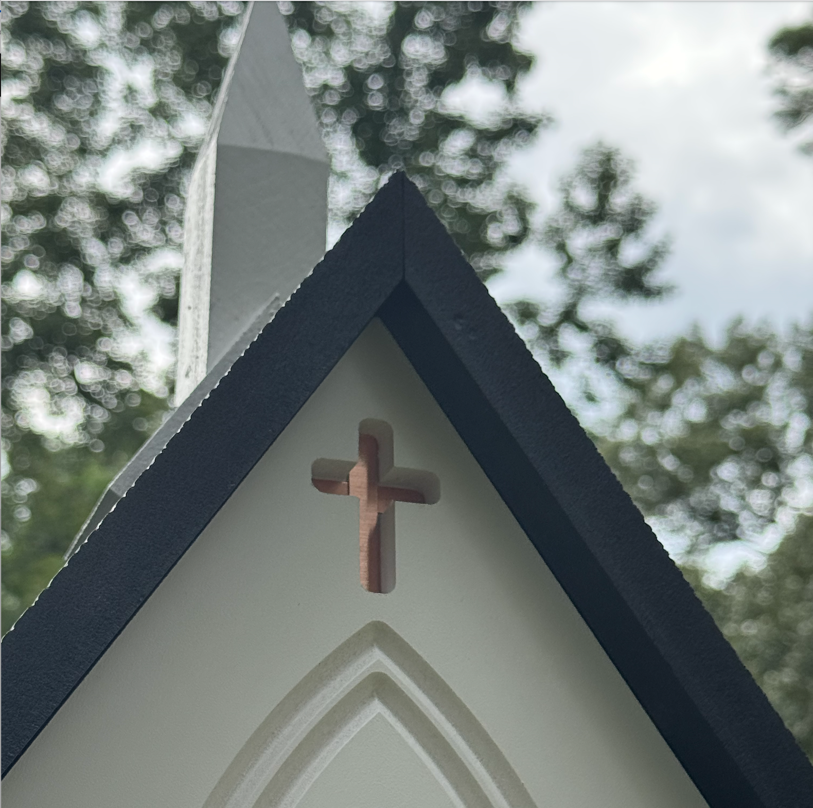 Cross on top of a church steeple with trees in the background