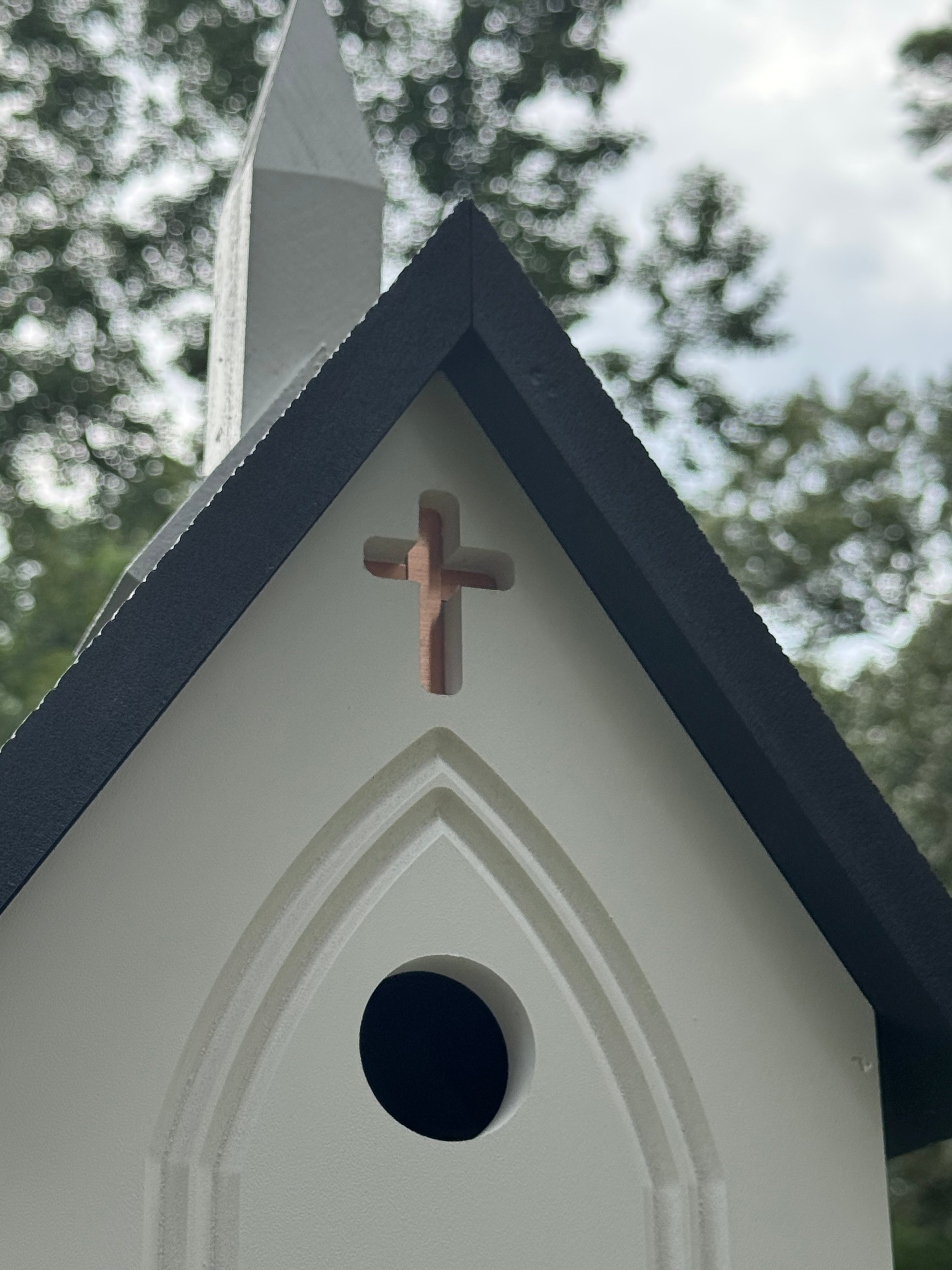 Gothic-style birdhouse with a cross on top against a blurred natural background