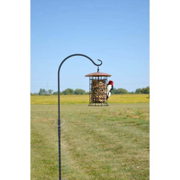 Bird feeder on a stand in an open field with a clear blue sky.