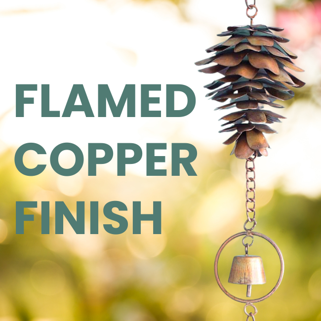 Two Copper Pine Melody wind chimes hanging outside on a porch, featuring detailed pine cone designs with flamed copper finish.