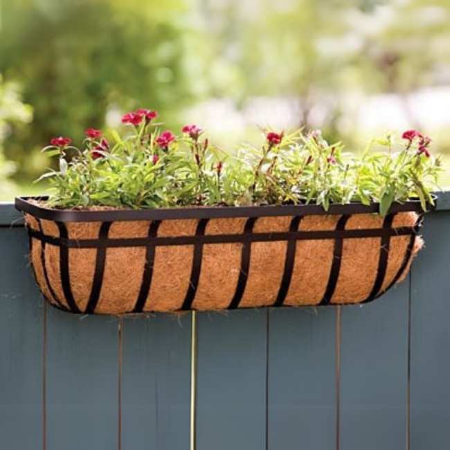 A deck railing planter attached to a wooden fence with vibrant flowers, adding beauty to an outdoor space
