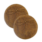 Two handcrafted dragonfly garden stepping stones with a rustic autumn wheat finish, placed along a path surrounded by colorful garden plants.
