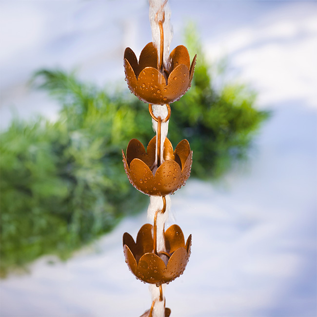The full length of the Floral Flow rain chain installed on a home’s gutter, guiding water from the roof with an elegant, copper-toned finish and creating a serene outdoor display.