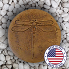 Close-up view of a dragonfly design on a round concrete garden stepping stone with an autumn wheat finish, placed on white gravel.