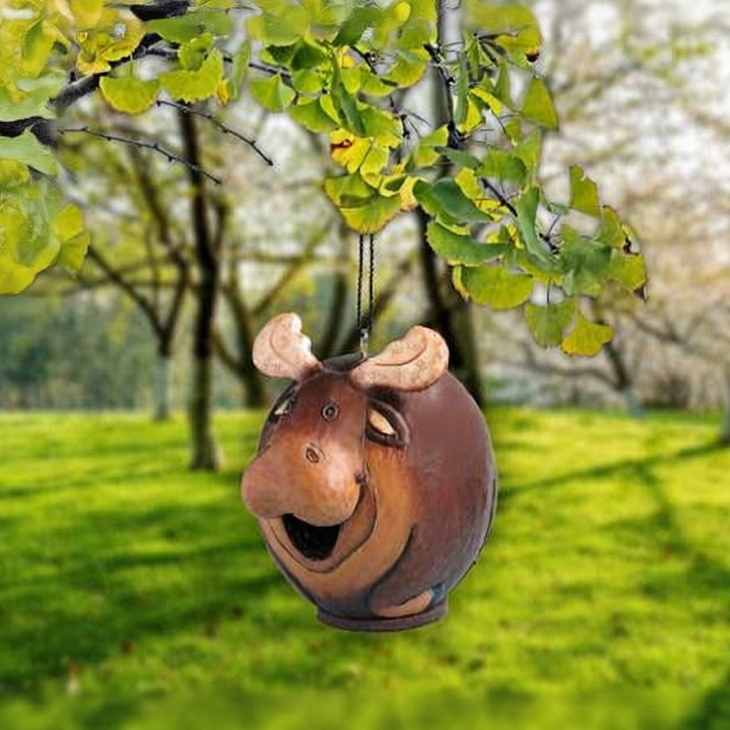 Moose-shaped birdhouse hanging from a tree in a garden setting