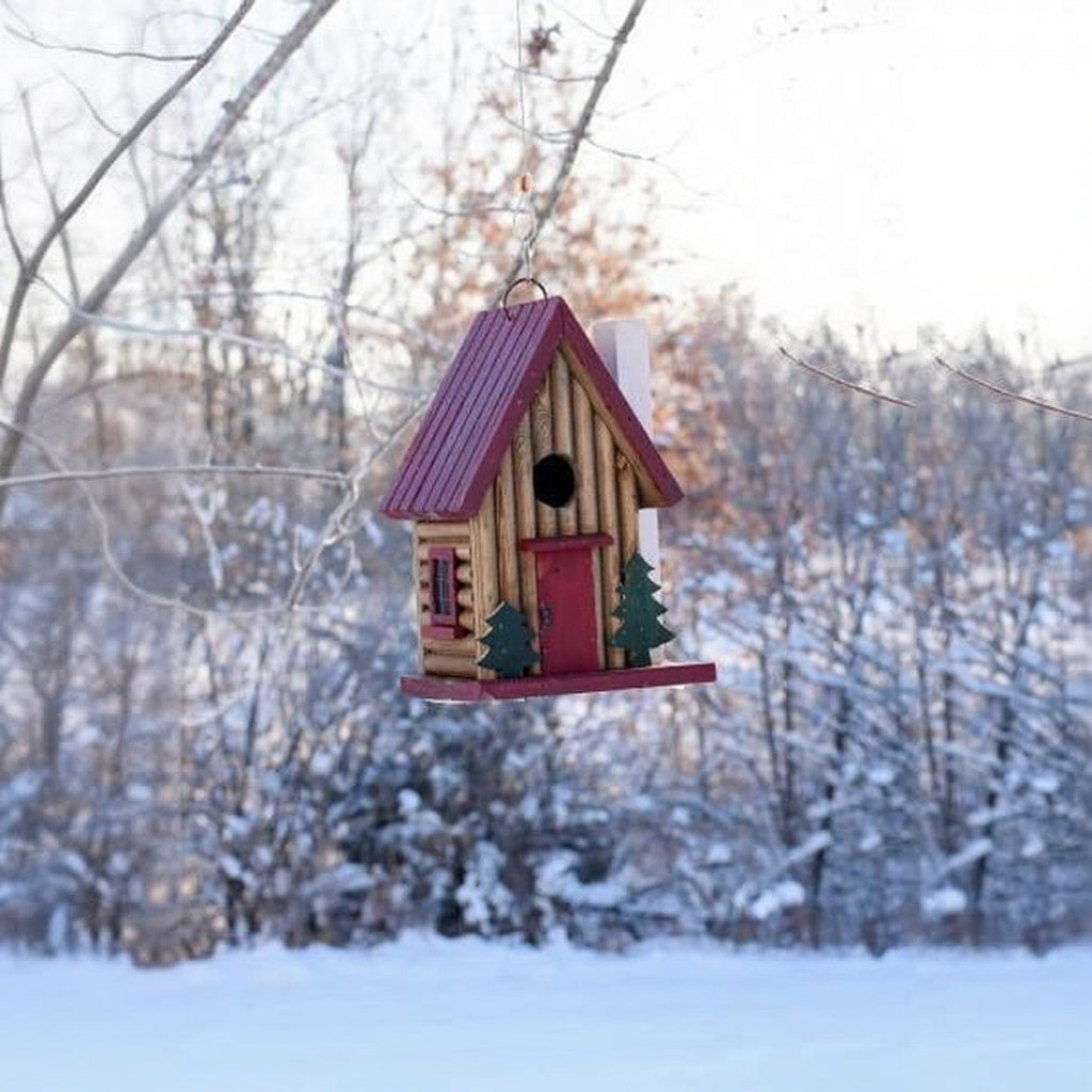 Birdhouse with a red door and green trees on a snowy background
