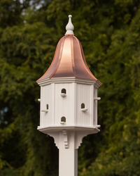 Decorative white birdhouse with a copper roof against a green foliage background