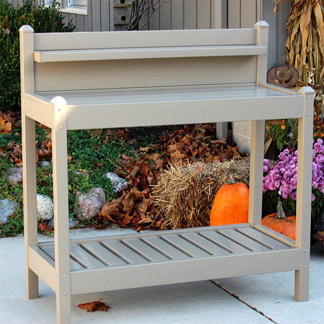 Potting bench with slatted bottom shelf for drainage, set against a backdrop of pumpkins and fall foliage.