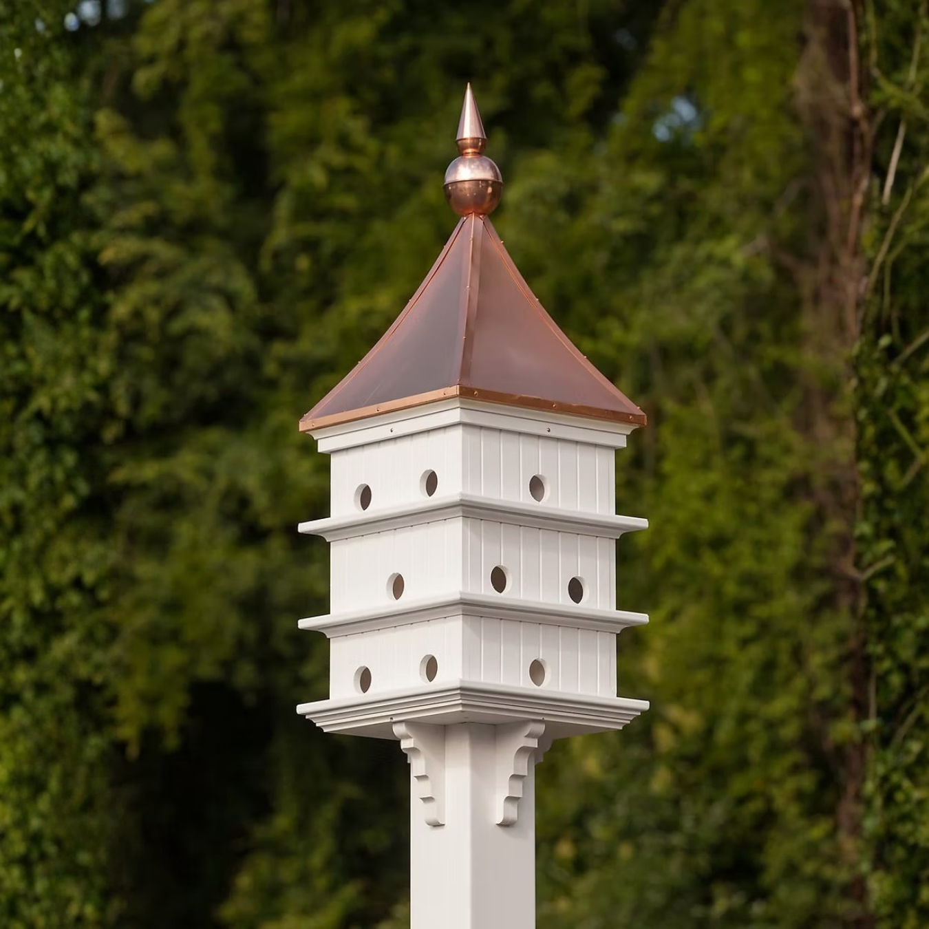 Classic Purple Martin white birdhouse with a copper roof against a green tree background